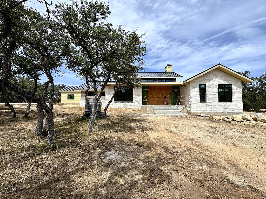 Real photo of the front of 168 Crooked Creek Court framed by mature live oaks, Johnson City, TX, September 2026
