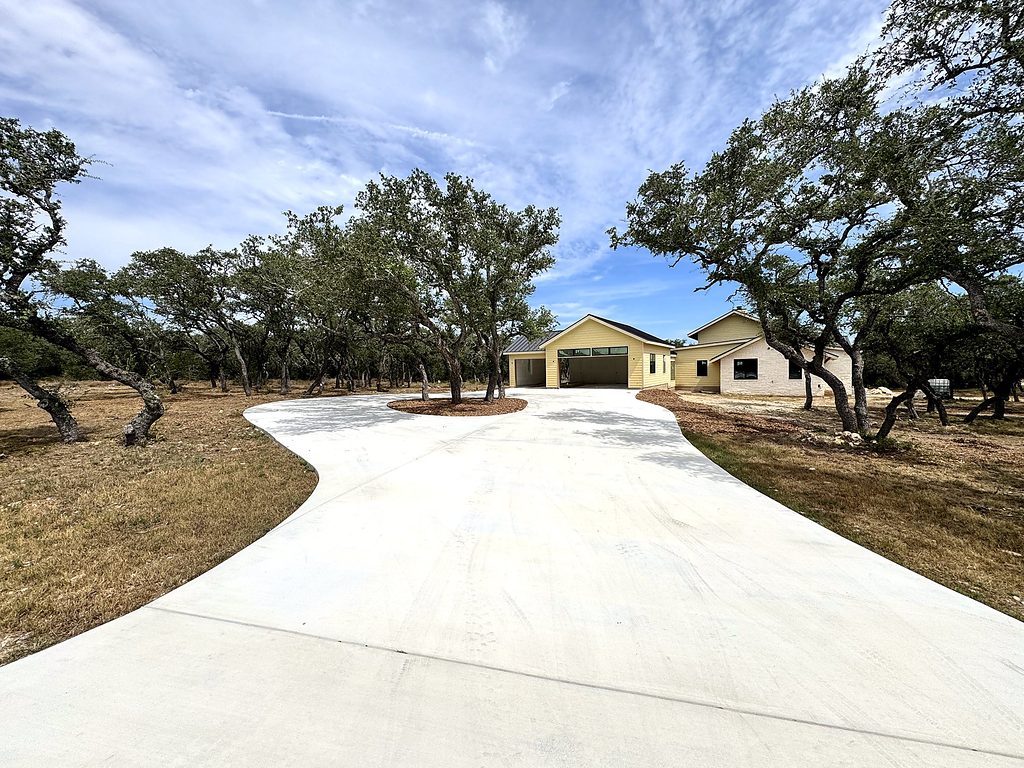 Real photo of the curving concrete driveway through live oaks to 168 Crooked Creek Court, Johnson City, TX, September 2026